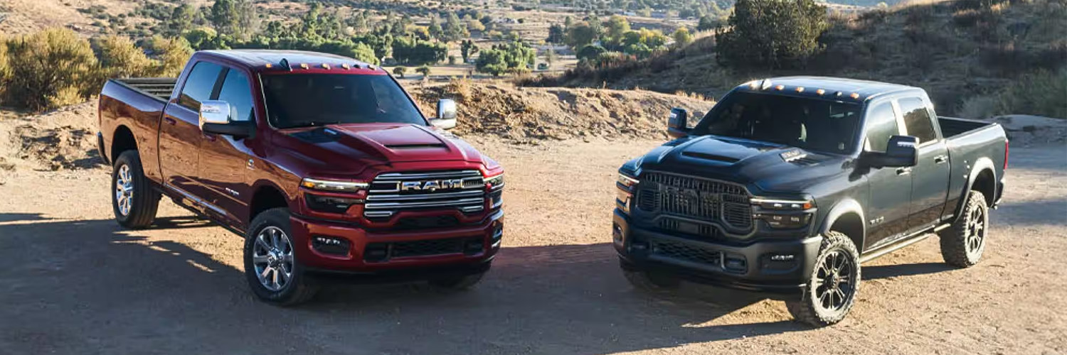 A red 2025 Ram 2500 Laramie 4x4 Crew Cab and a black Ram 2500 Rebel 4x4 Crew Cab parked on a clearing in the mountains.