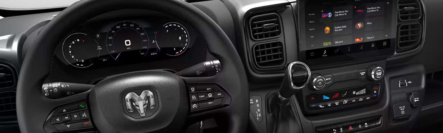 A close-up of the interior of the 2025 Ram ProMaster, focusing on the steering wheel, Digital Cluster Display, Uconnect touchscreen and climate controls.
