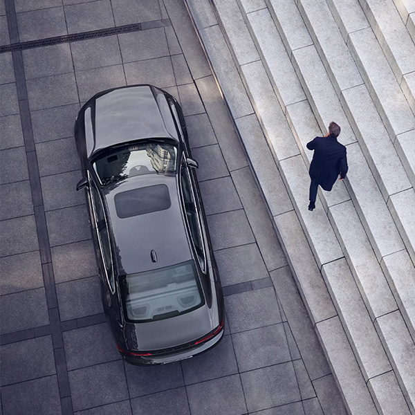 A Volvo S90 is parked in front of a set of stairs, a man walks away from the car.