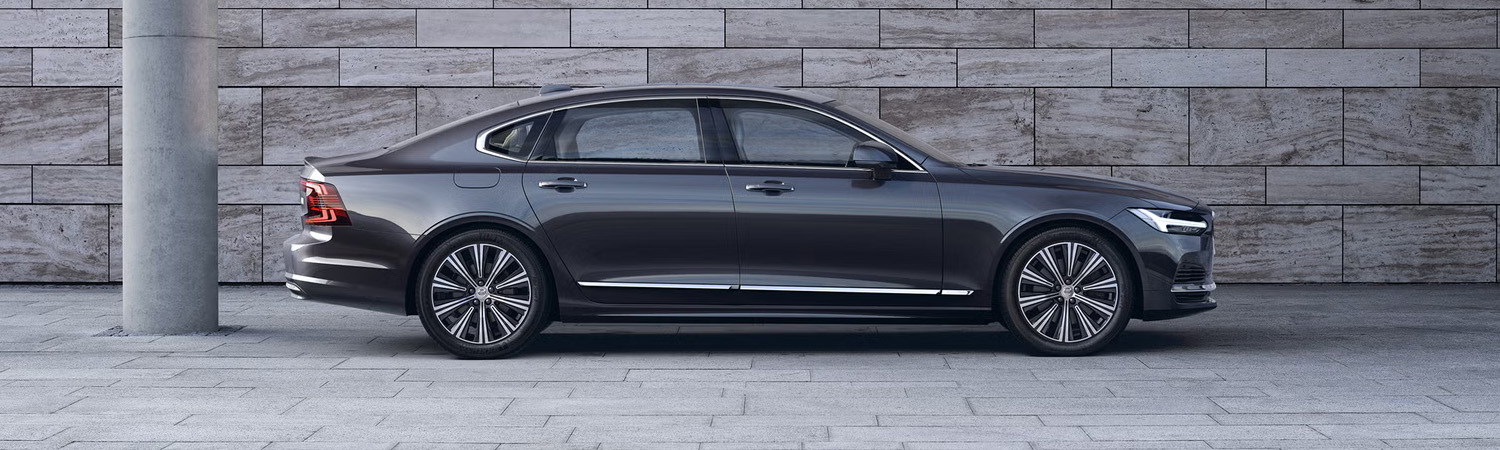 Volvo S90 seen from side parked in front of gray concrete wall.