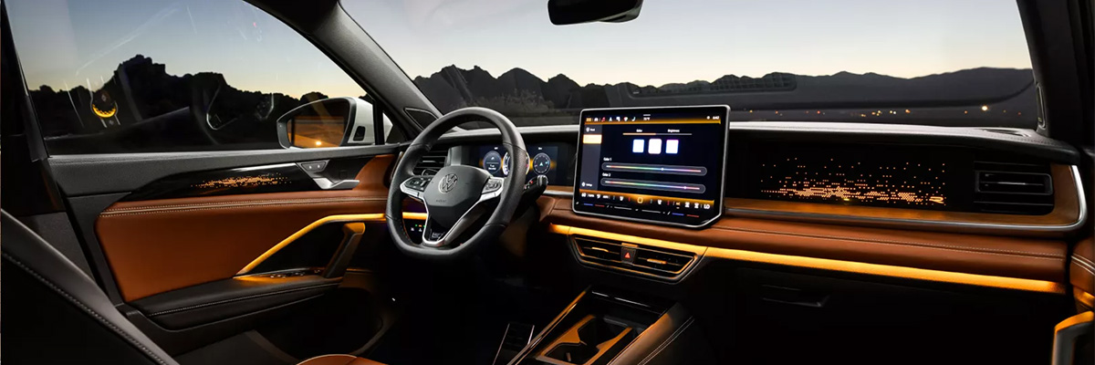 Interior view of a Tiguan shown in available Amberbraun leather highlighting the available interior ambient lighting with mountains visible in the distance through the windshield.