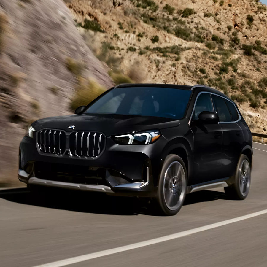 Shot of the 2026 BMW X1 xDrive28i SUV driving on a curvy road in a mountainous setting