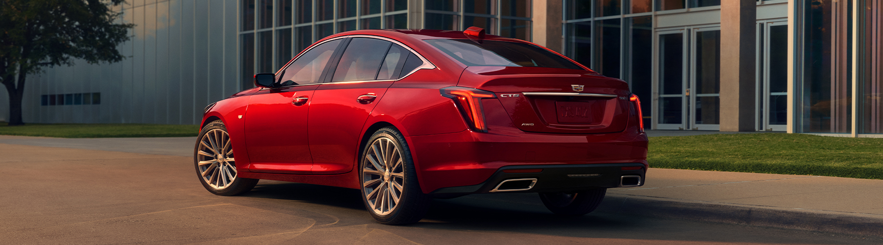 A Driver Side Rear View of a Red 2026 Cadillac Parked Near an Industrial Building