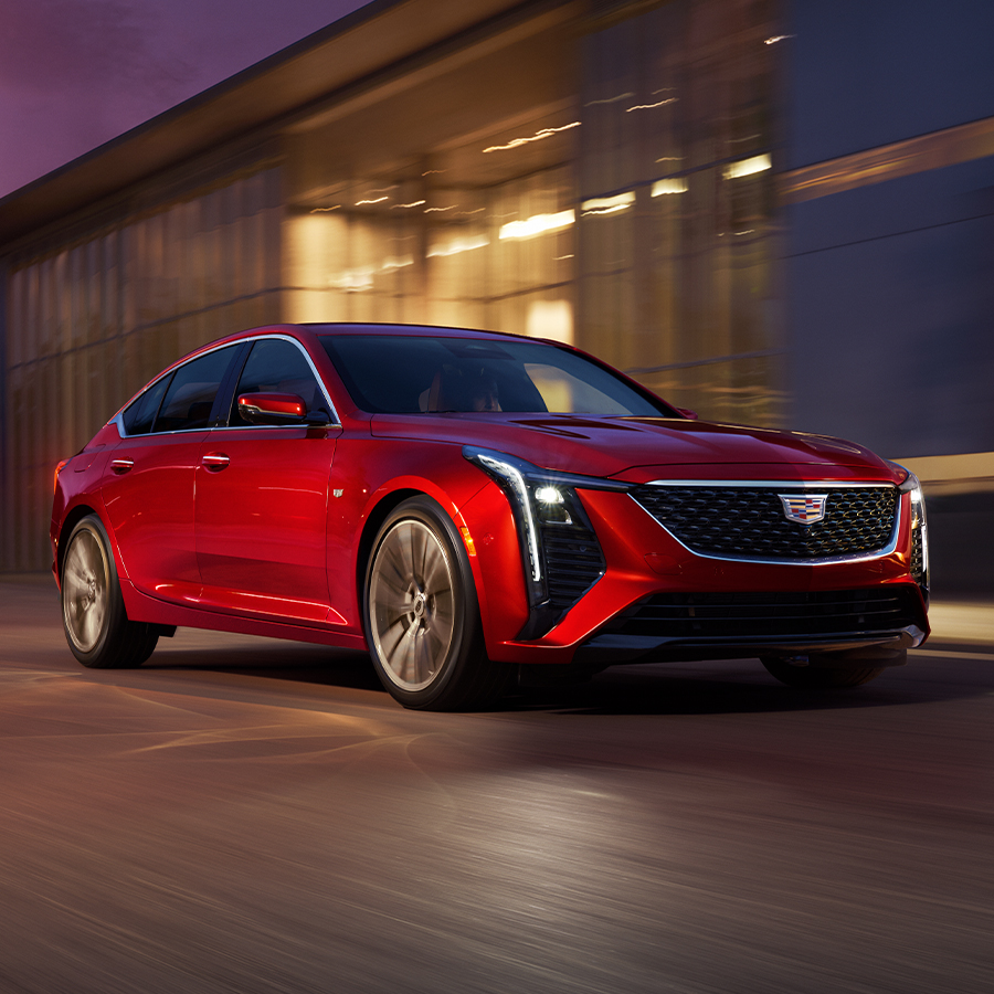 Front View of Red 2026 Cadillac CT5 Driving Past an Industrial Building