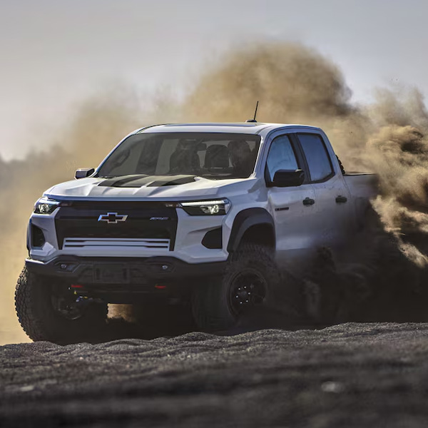 Three Quarters View of a White 2026 Chevy Pickup Truck Driving Though the Desert with Dust and Sand Flying Behind