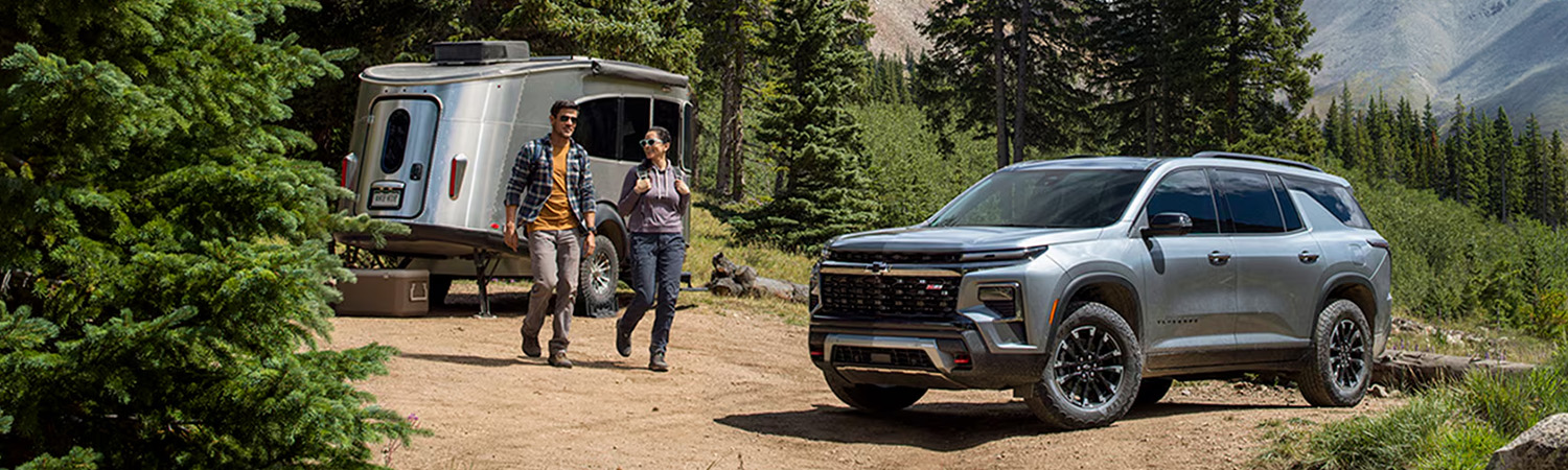 2026 Chevy Traverse parked on a dirt road towing an Airstream trailer with two people walking nearby in the mountains