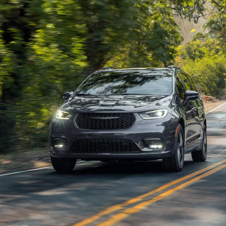 Front profile of the 2026 Chrysler Pacifica driving on a scenic coastal road at sunset.