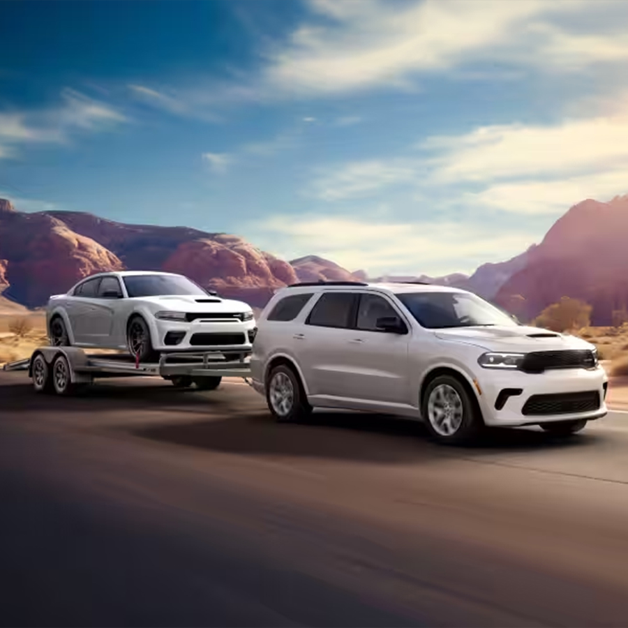 2026 Dodge Durango towing a performance car on a trailer through a desert highway landscape.