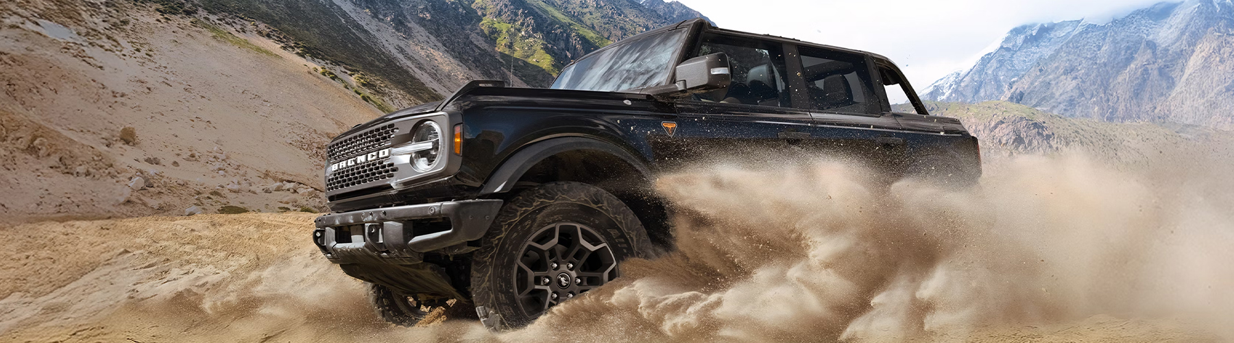 A 2026 Ford Bronco® SUV kicking up dust in a valley beneath rocky hills
