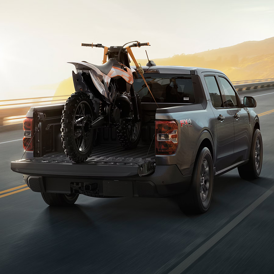 2026 Ford Maverick® Tremor® model with a motorcycle strapped in the bed being driven on the highway