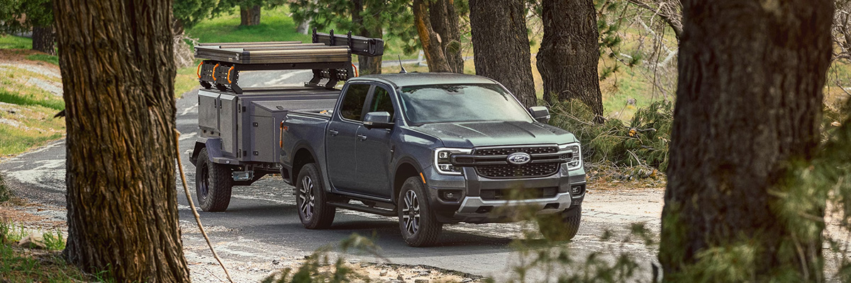 A 2025 Ford Ranger® in Cactus Gray towing a trailer through a wooded road
