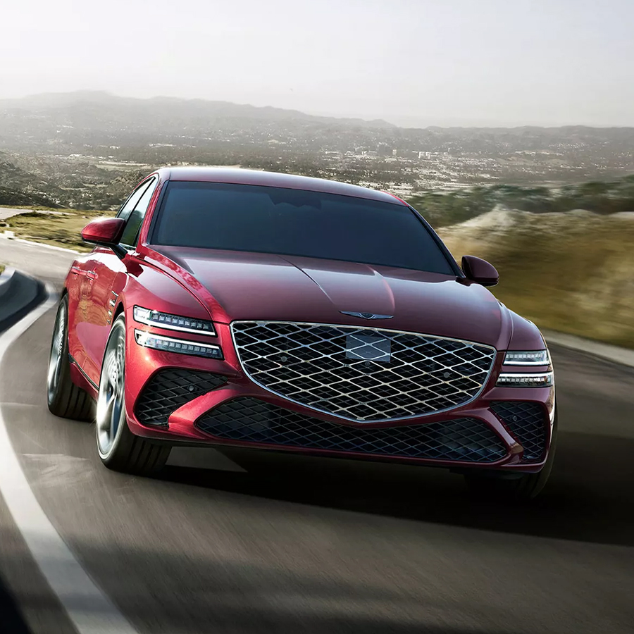 G80 driving down curving highway road, front view showcasing bold grille and sleek headlights