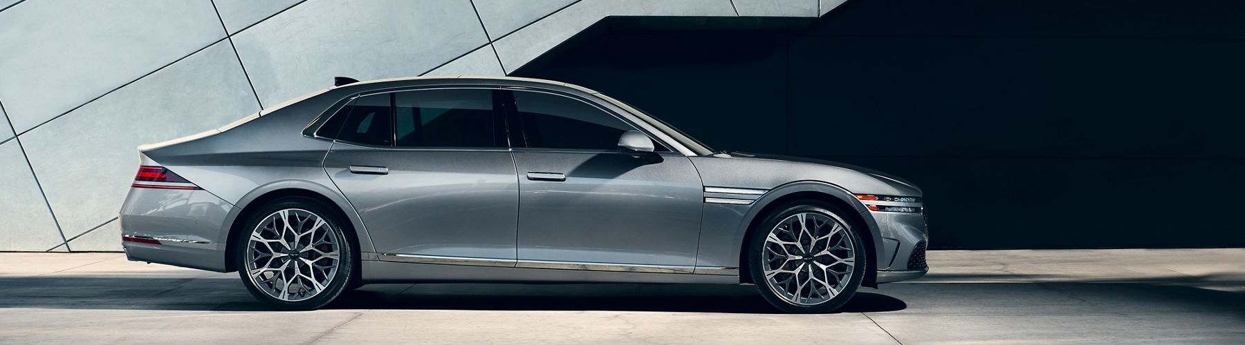 Exterior passenger side profile view of 2026 Genesis G90 in Savile Silver next modern metal building