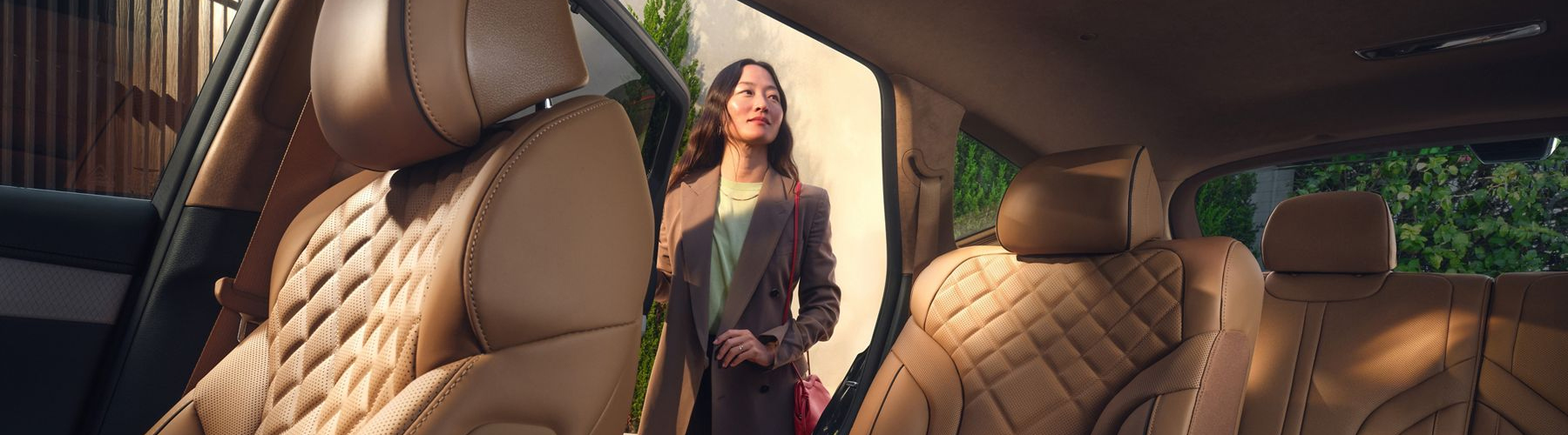 Front driver side POV of Genesis GV80 rear interior with tan quilted leather seats & open rear door