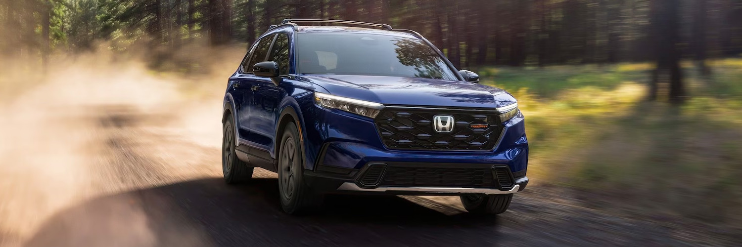 Exterior shot of a 2026 Honda CR-V driving on a dirt road in the woods.