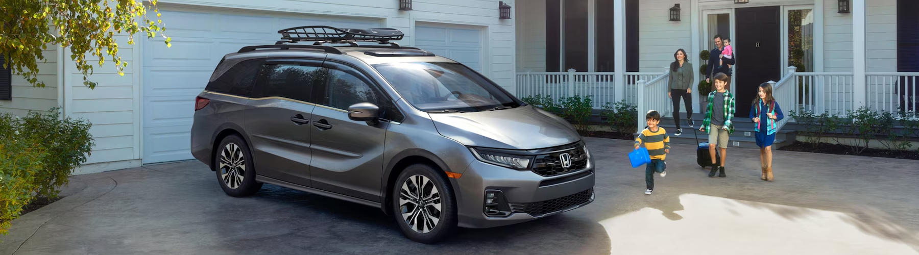 2026 Honda Odyssey Elite in Modern Steel Metallic with accessories parked in front of a house with family walking to the vehicle.