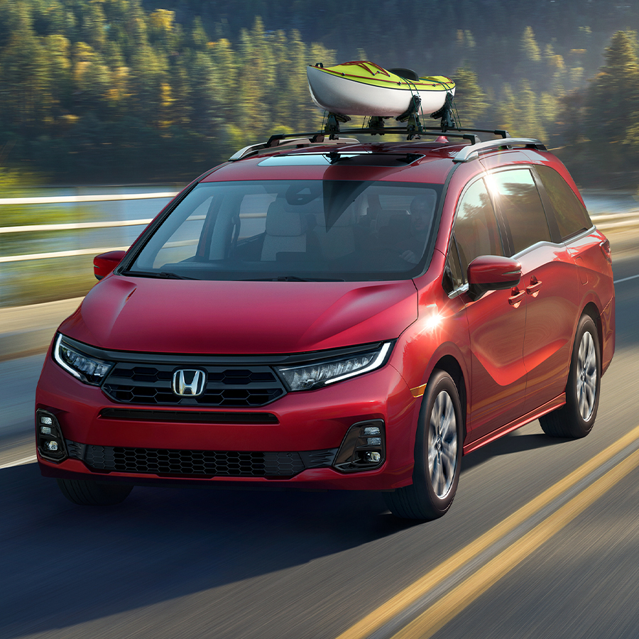 2026 Honda Odyssey Elite in Radiant Red Metallic II driving at sunrise with mountains and trees in background.