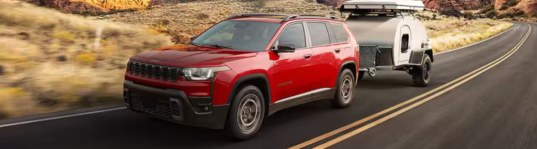 Display A red 2026 Jeep Cherokee Limited traveling down a highway, towing a small travel trailer.