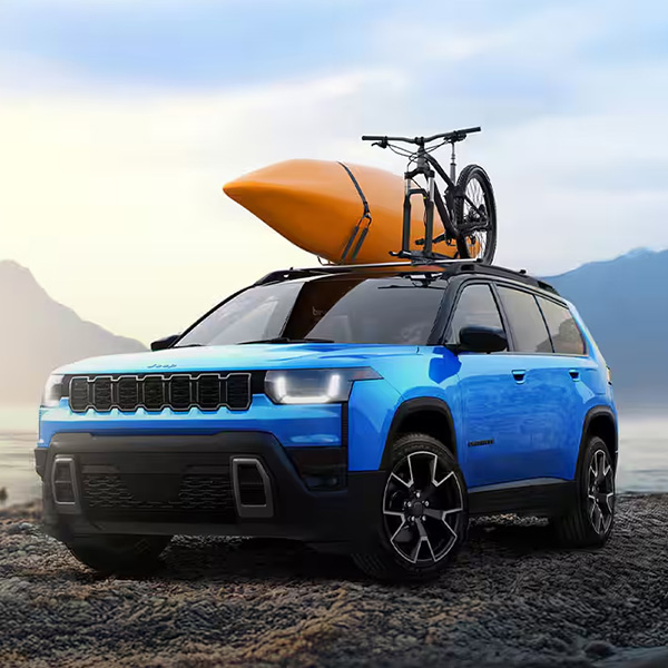 Blue 2026 Jeep Cherokee parked by a lake with a kayak and bike mounted on the roof rack.