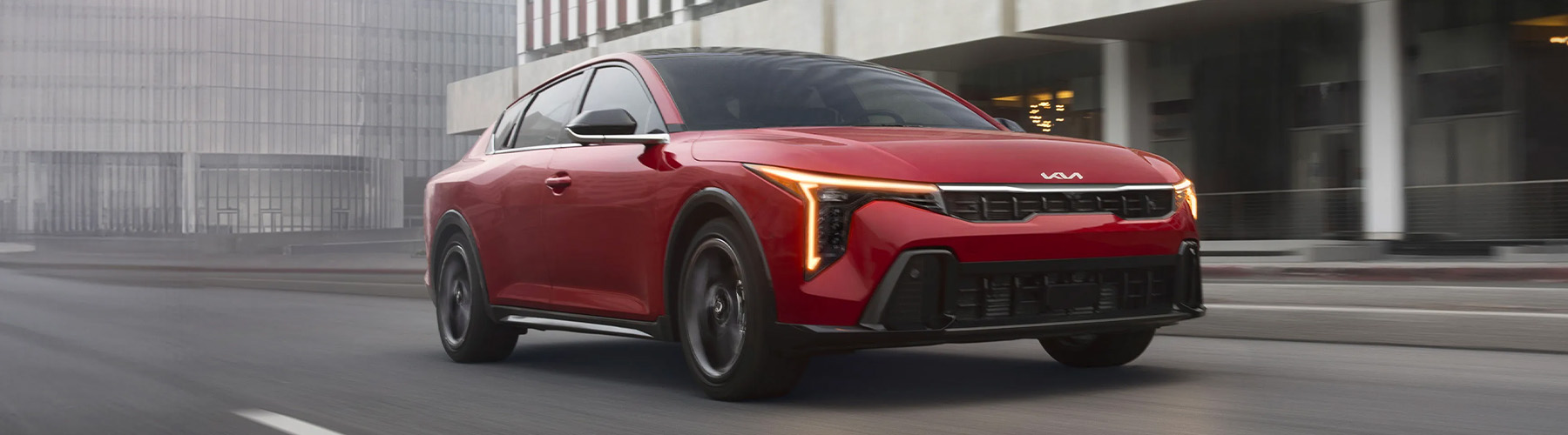Dynamic shot of the 2026 Kia K4 sedan in red, looking stylish as it drives through an urban city environment