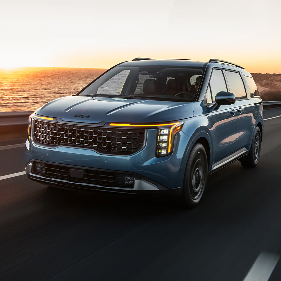 2026 Kia Carnival MPV in blue, three-quarter front view, highlighting the vertical LED headlights and sleek grille