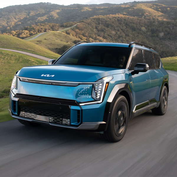 Blue 2026 Kia EV9 racig down a scenic highway