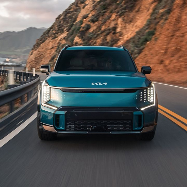 Blue 2026 Kia EV9 driving down a road with hills