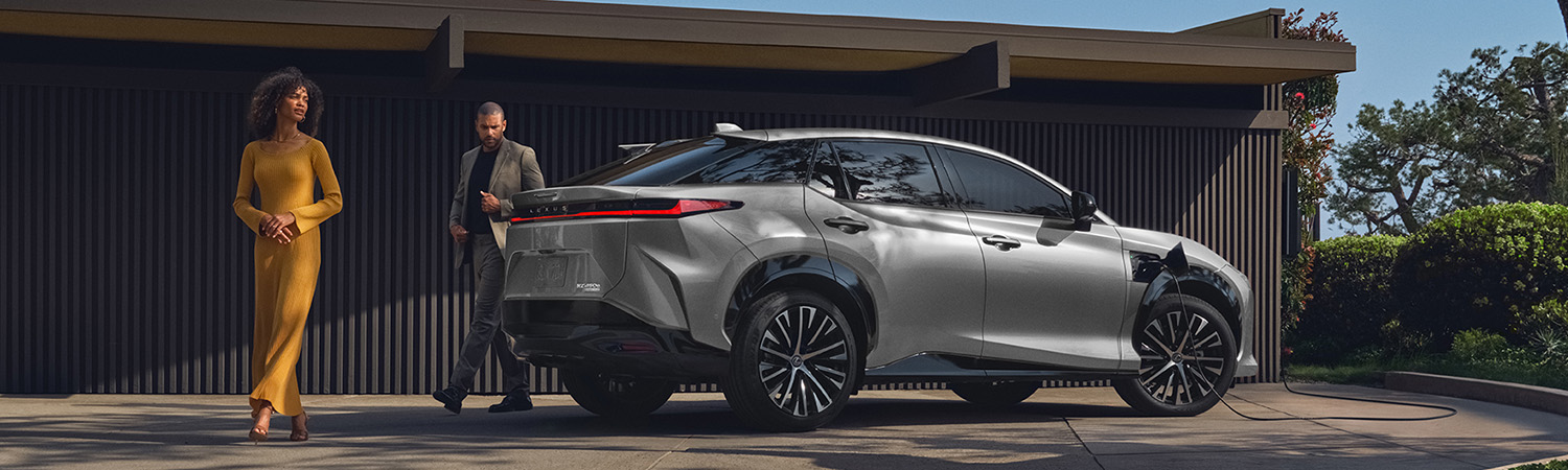 A side view profile of the 2026 Lexus RZ showing the new North American Charging System (NACS) port located on the passenger-side front fender, complemented by 20-inch black aero-cover wheels.