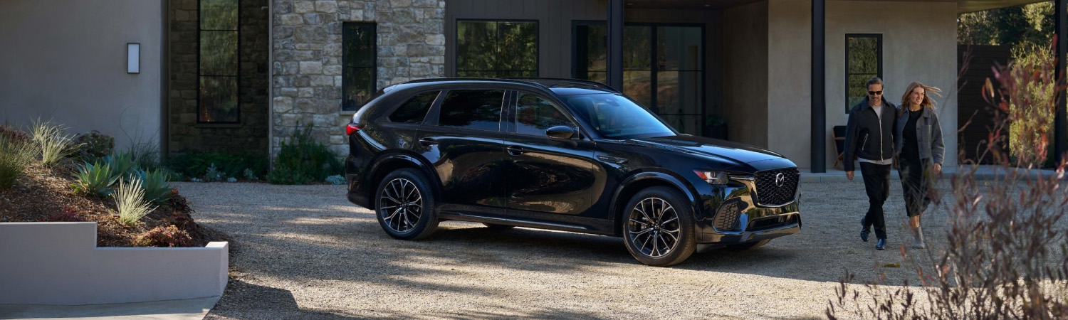 Black Mazda CX-70 parked in a residential driveway with a couple walking nearby.