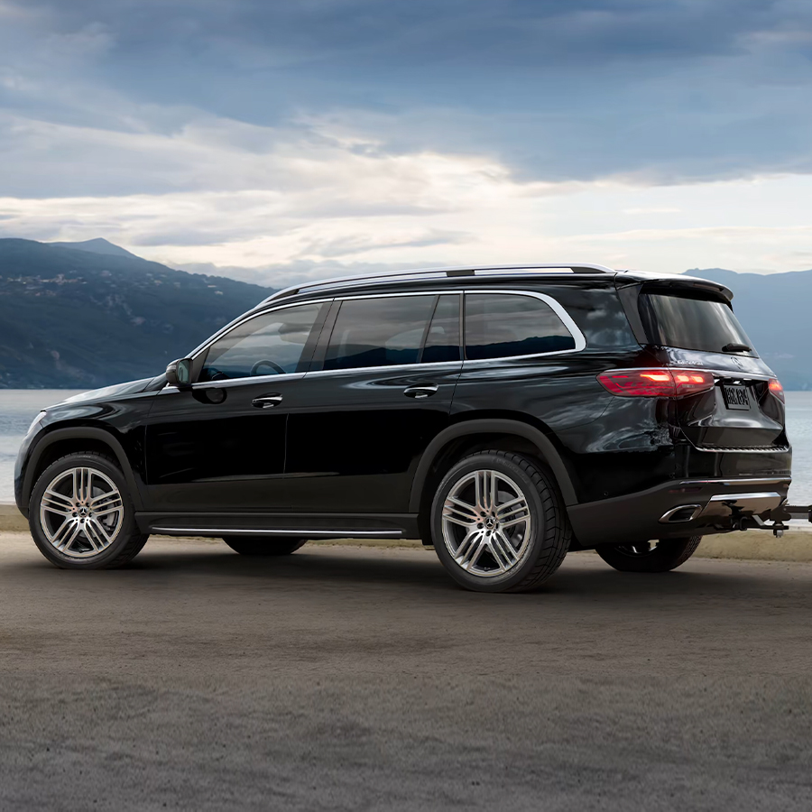 2026 Mercedes-Benz GLS in black viewed from rear three-quarter angle on an open road with mountains