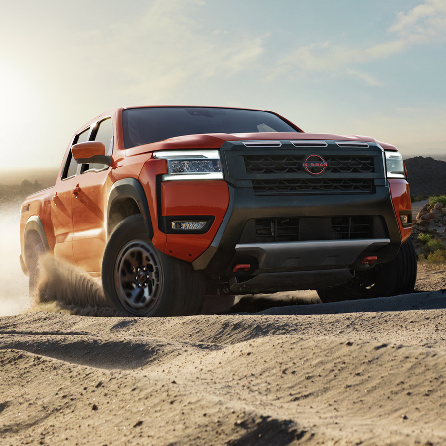 2026 Nissan Frontier in red, 3/4 front view driving on a dirt road kicking up dirt