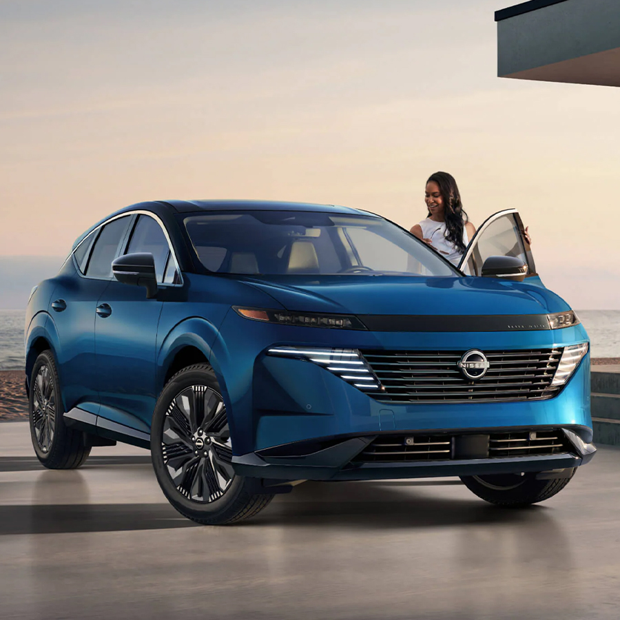 2026 Nissan Murano 3/4 front view with woman at driver's door, outside oceanside home