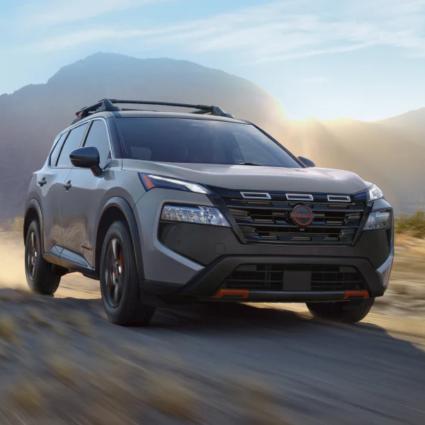 2026 Nissan Rogue driving down a dirt road with mountains behind