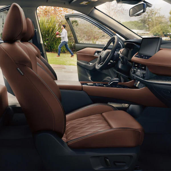 Interior view of the 2026 Nissan Rogue cabin featuring luxurious chestnut brown leather seats, a center console, and a large central display screen, showing the premium comfort and technology.