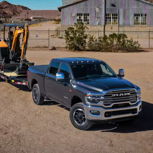 A black 2026 Ram 2500 Laramie at a desert ranch towing an excavator on a flat bed trailer.