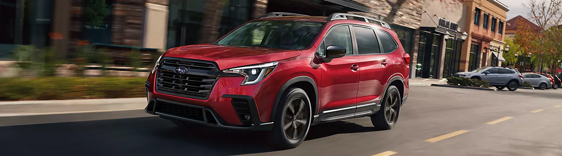 A red 2026 Subaru Ascent drives out of a strip mall parking lot.