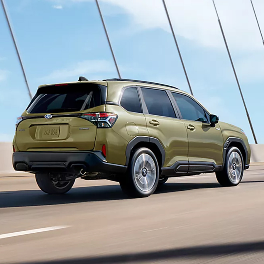 A 2026 Subaru Forester Hybrid in Autumn Green Metallic drives across a suspension bridge.