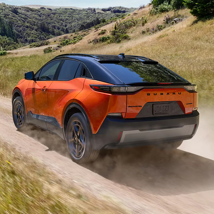Rear driver-side view of a Subaru EV SUV heading down a mountain road