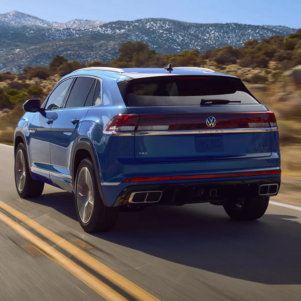 Rear view of an Atlas Cross Sport shown in Mountain Lake Blue driving on a road with mountains in the background