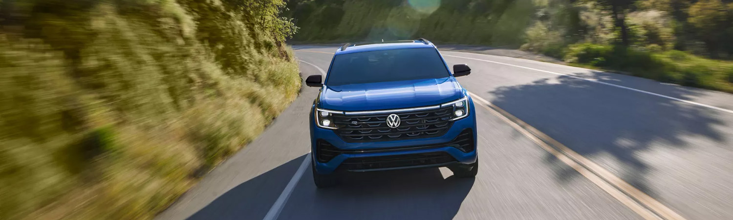 Aerial shot of an Atlas Cross Sport shown in Mountain Lake Blue driving on a wooded mountain road.