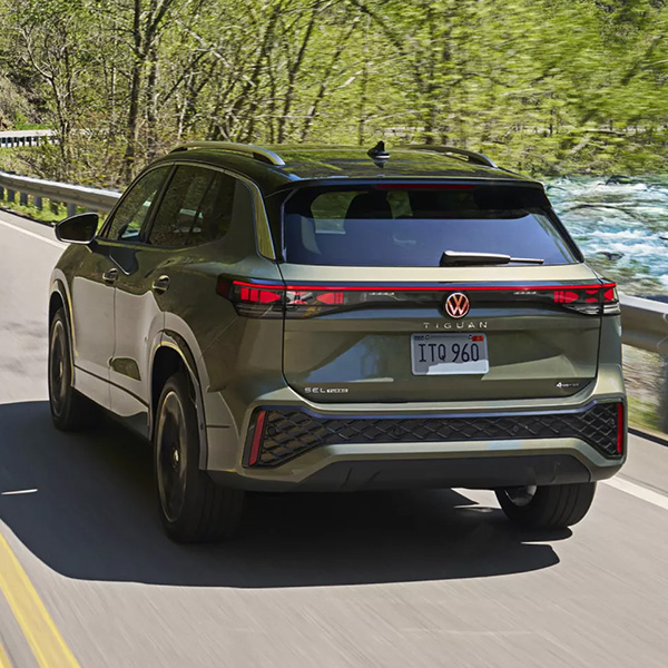 Rear exterior shot of a 2026 Volkswagen Tiguan driving on a road alongside a stream.