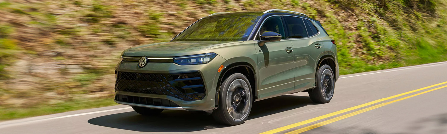 Exterior shot of a 2026 Volkswagen Tiguan driving on a road with a hill in the background.