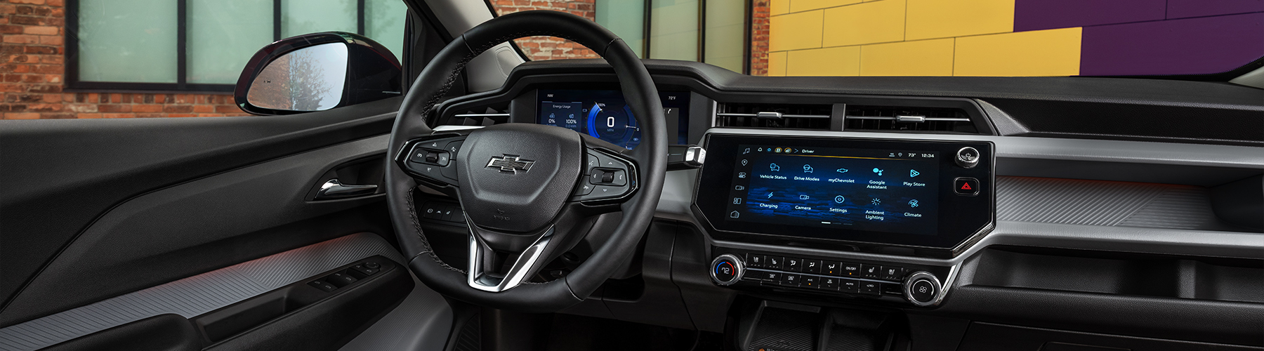 The Chevrolet 2027 Bolt RS interior is featured in Black with Red Stitching (HXR) in an urban setting at daytime.