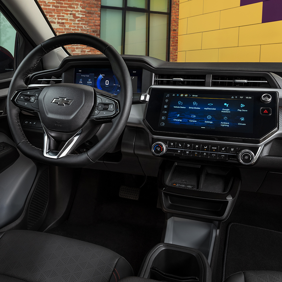 The Chevrolet 2027 Bolt RS interior is featured in Black with Red Stitching (HXR) in an urban setting at daytime.