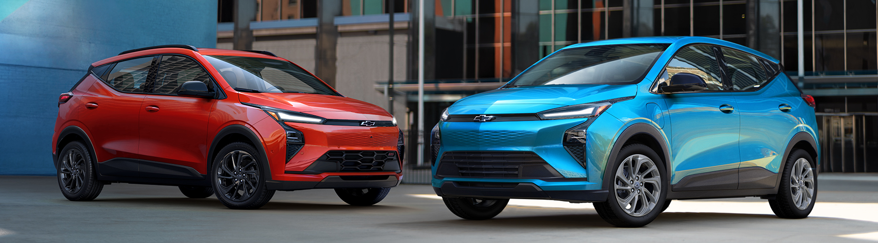 2027 Chevrolet Bolt Pack shot in a colorful urban city setting with a glass building and American flag in the background. Showcasing the RS and LT trims.