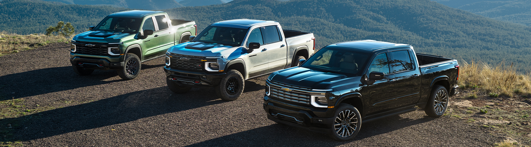 The Sun Shining on Three Chevy Silverado 1500 Trucks Lined Up at the Top of a Mountain
