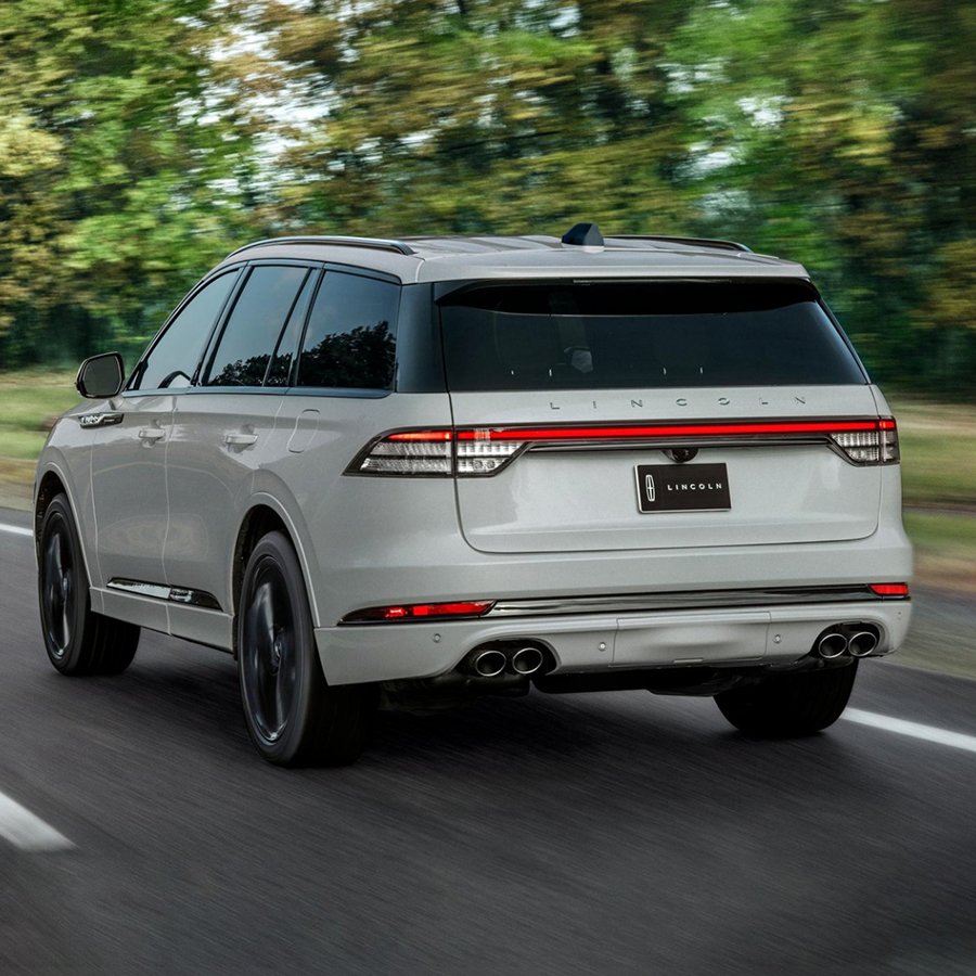 Rear view of a 2027 Lincoln Aviator® SUV is being driven on a country road