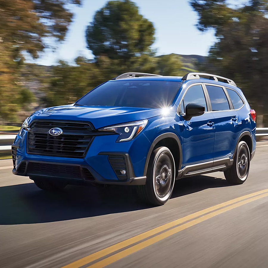 2027 Subaru Ascent 3-row SUV drives on a rural highway.