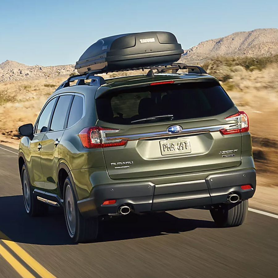 2027 Subaru Ascent AWD SUV with a Thule roof cargo carrier drives on a desert highway.
