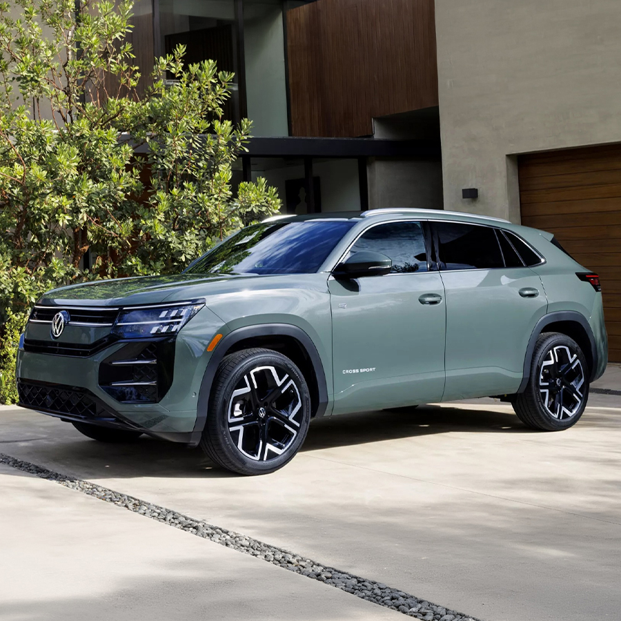 An Atlas Cross Sport shown in Dark Sage Metallic parked in the driveway of an upscale house.
